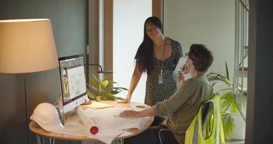 A caucasian man and asian woman in an office are video calling a construction worker