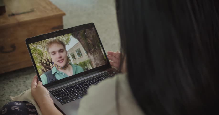 A girl receives a video call on a laptop while sitting in a couch at home