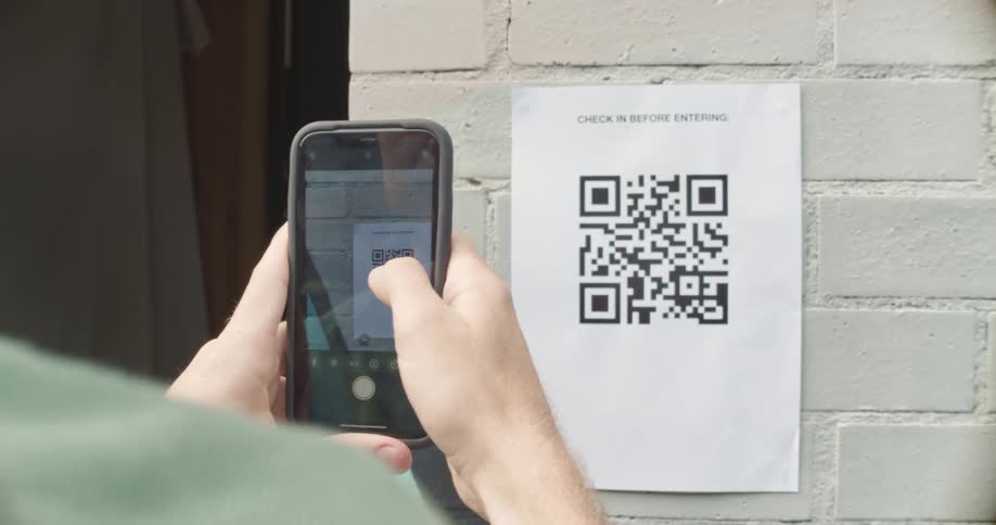 A person uses a smartphone to scan a qr code posted on the facade of a building during the day