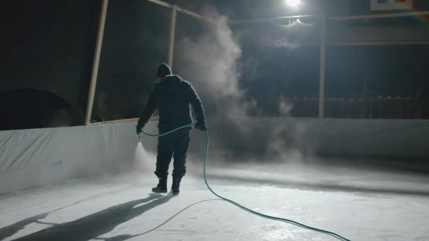 A man hoses the floor in the interior of a construction site with a coating