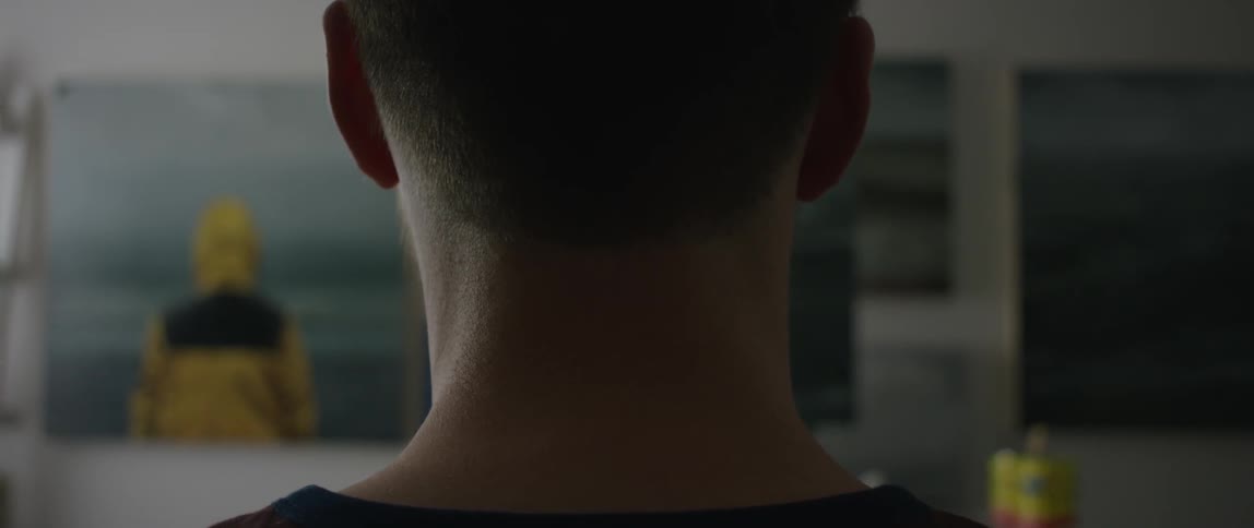 Back of man's neck as he faces a wall with art work