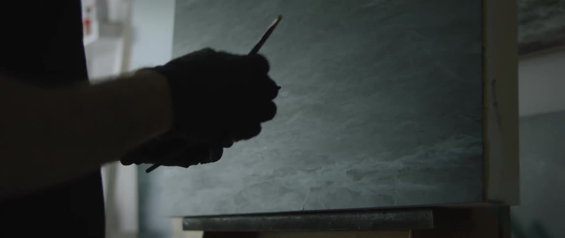 An artist stands at an easel with paint brushes in hand
