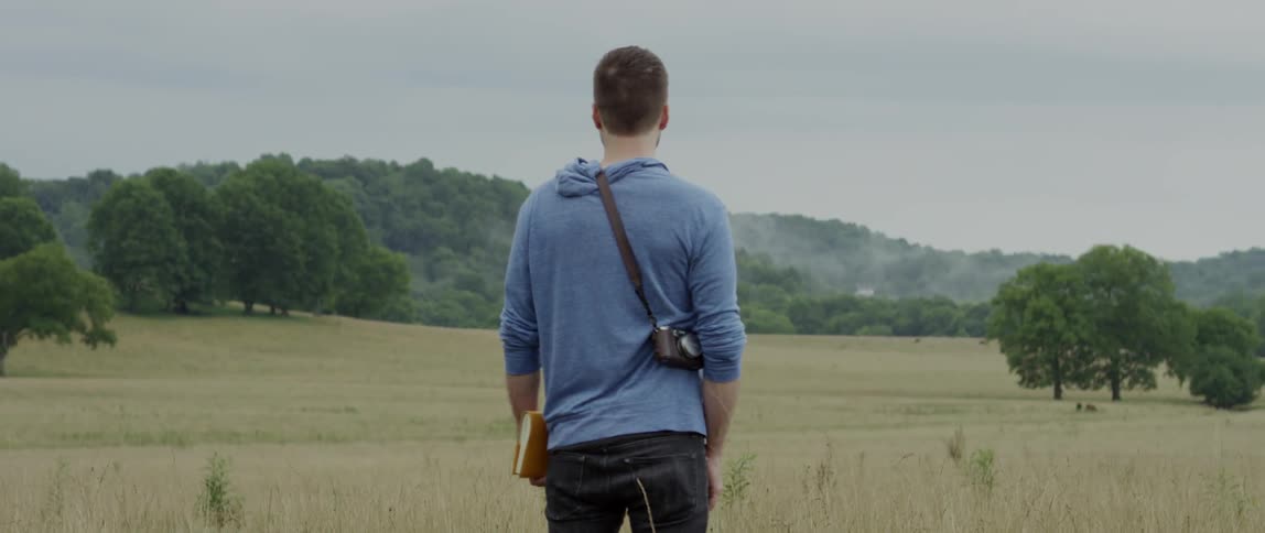 Man stands in a rural field with a notebook in hand