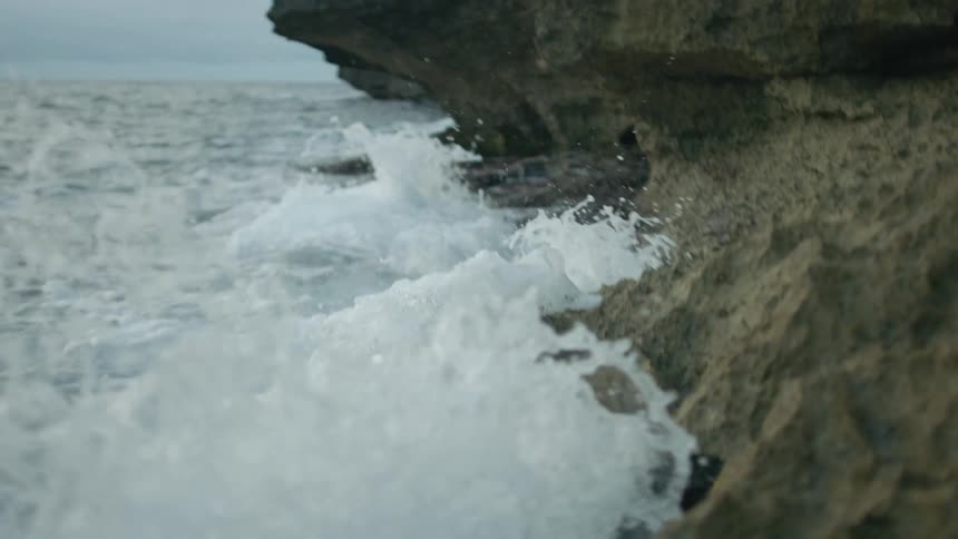 Waves splashing against coastal bluff with high cliff on a cloudy day