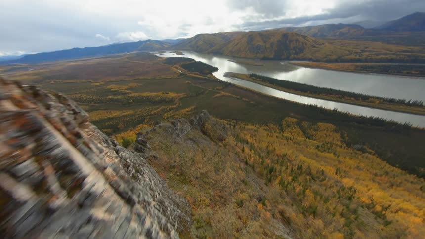 A mountain ridge looming over a verdant grassland and the river running through it during the day