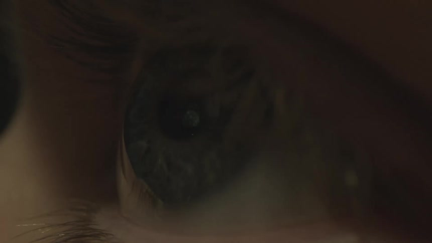 A persons eye is seen as they are staring straight at ahead and the color of nearby lights change