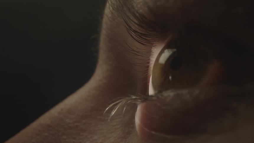 Close up of a womans hazel eye moving reading in a dark room