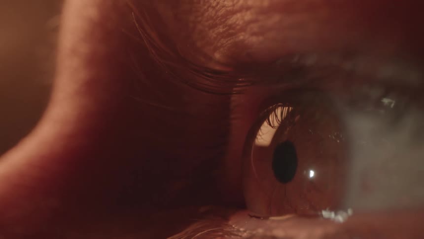An extremely tight close up of a persons eye shows them looking around at their surroundings