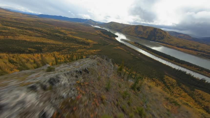 A cliff with trees with a river mountain range the sky and clouds in the background