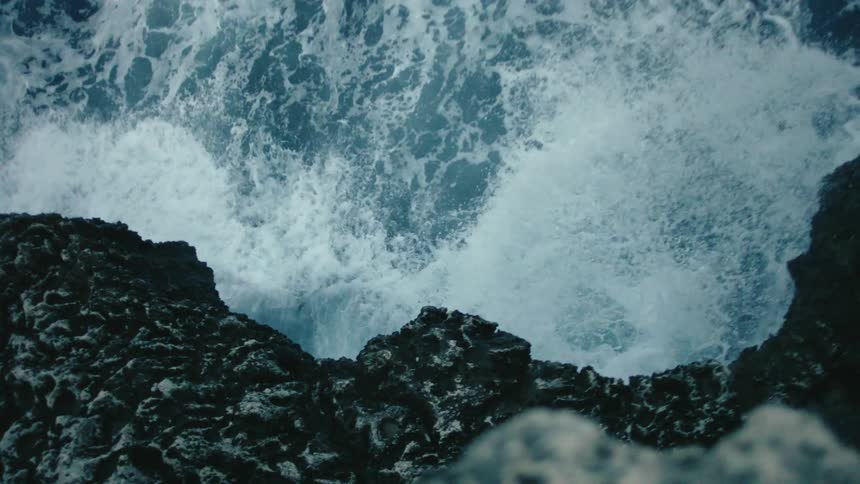 Ocean waves crashing under the dark rocks in a steep jagged cliff on the coast