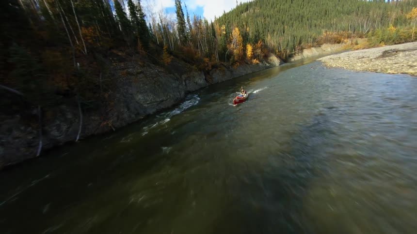 A man standing on a canoe floating down a river next to a forest