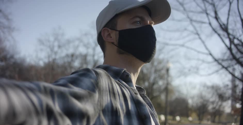A man with a mask on sits down on a park bench