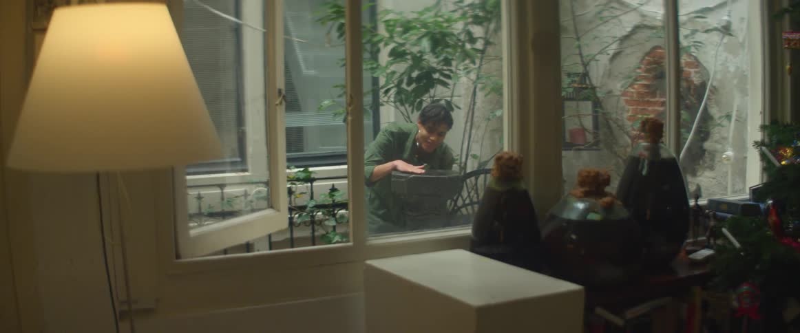 A person on a balcony with a room windows and a lamp in the foreground