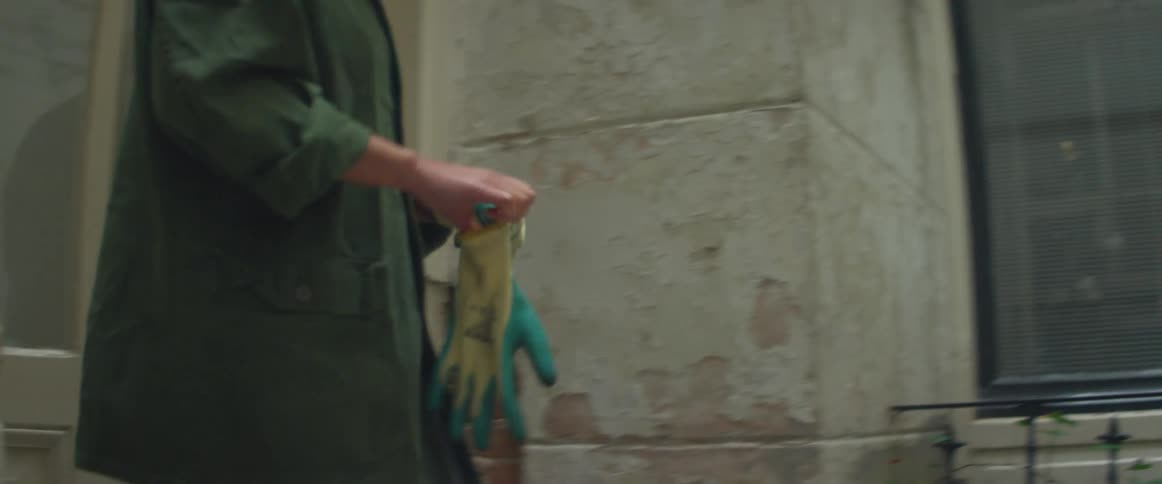A woman puts gardening gloves on as she walks outside of her home and heads to a plant
