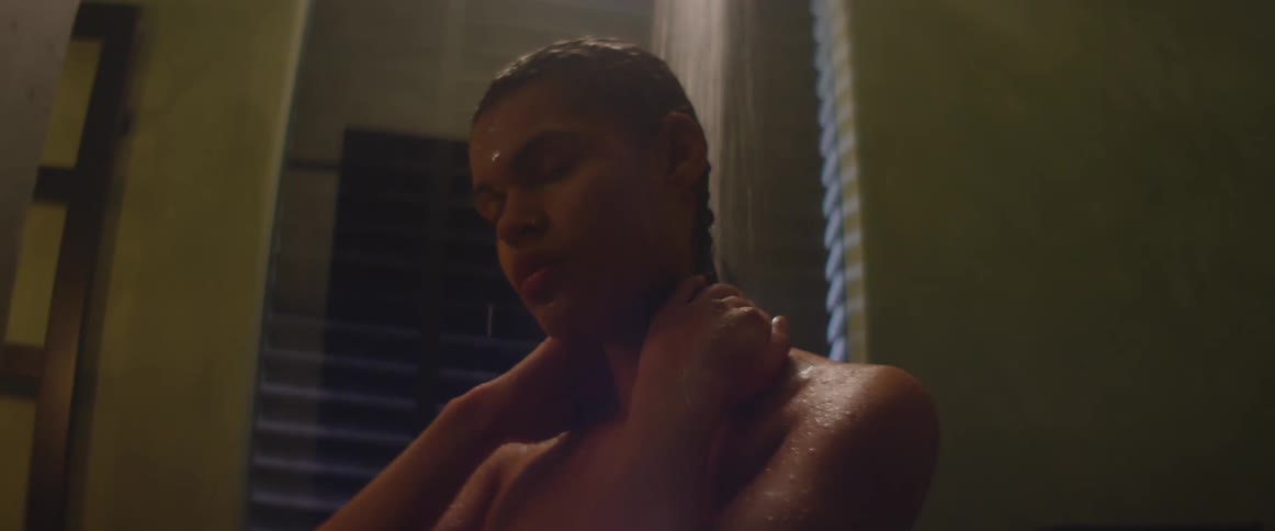 A young woman runs her hands through her hair as she showers in front of a covered window at night
