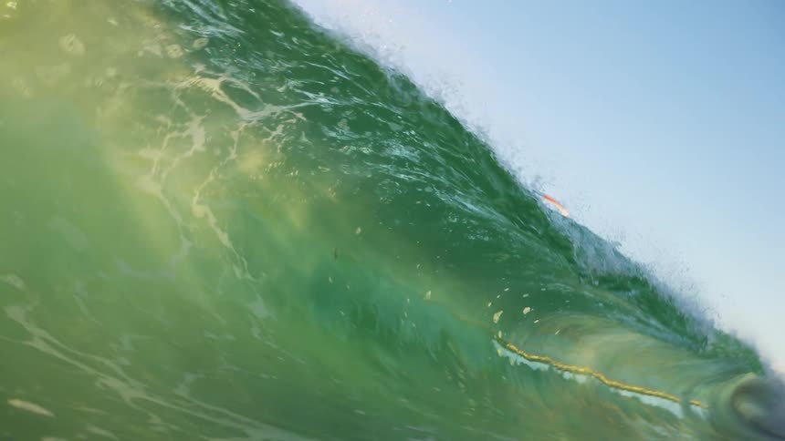A large wave moves across the ocean as a person parasails above