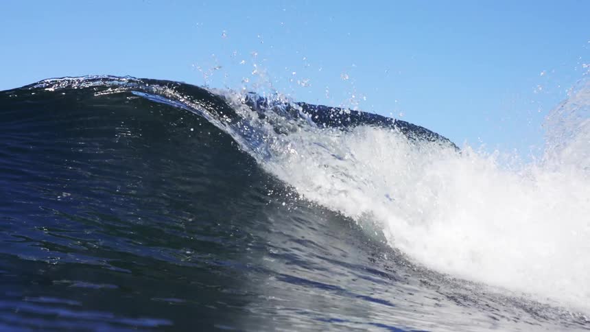 A wave crests in the ocean off a shoreline