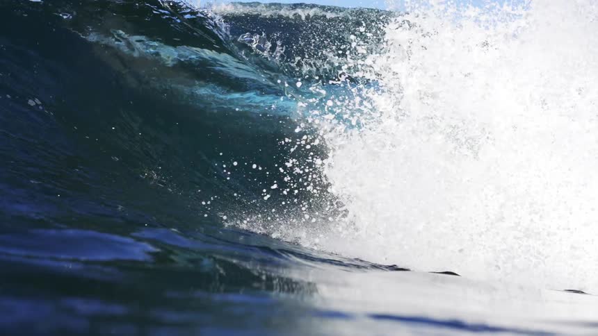 Ocean wave rolls in splashing on a clear day