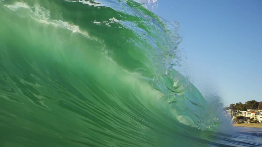 An ocean wave curls and breaks on a bright blue sky day