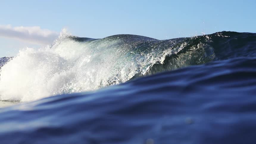 A large ocean wave crests and crashes on a sunny day