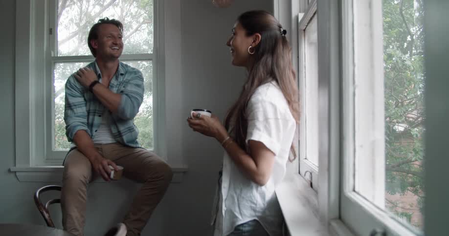 A man and woman talk and laugh as they drink coffee at home