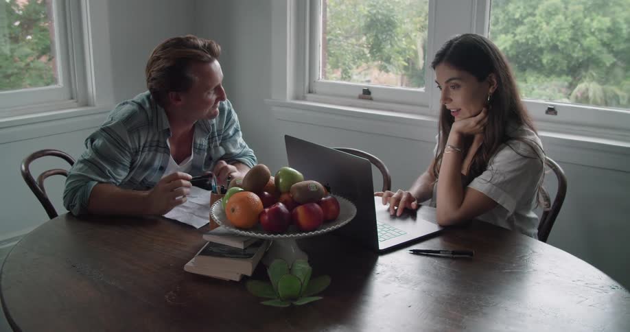 Young couple working from home sit on the dinning table with a laptop while talking