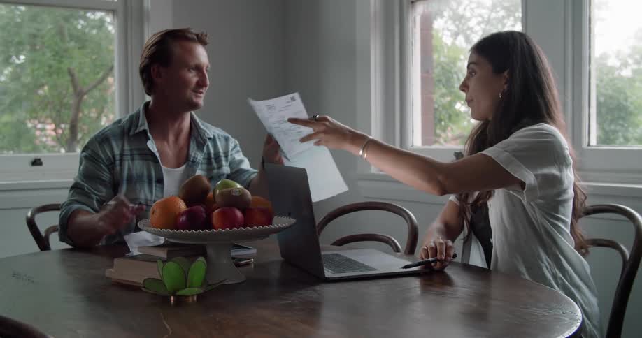 A man and woman sit at table at home looking at paper and a laptop in front of them