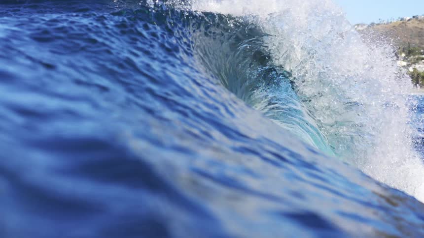 A large wave in the ocean with a neighborhood on the shore