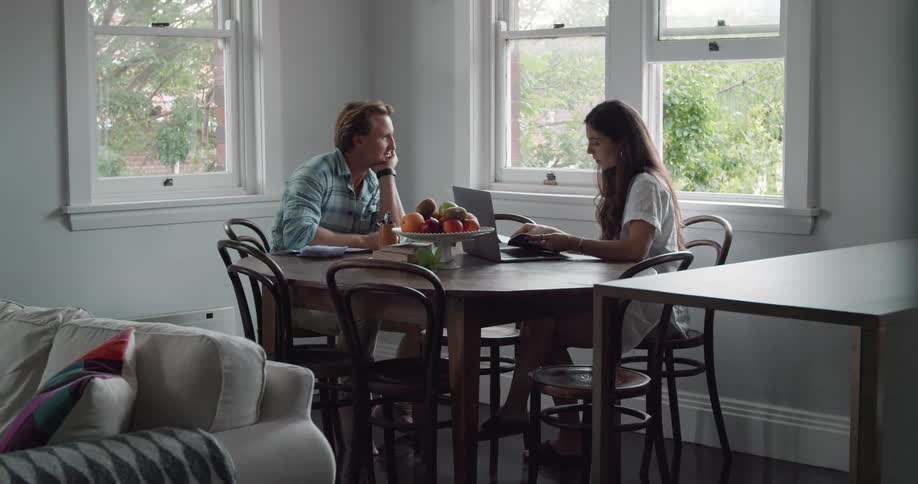 Woman uses a laptop while sitting at a table with a man who hands her a notebook