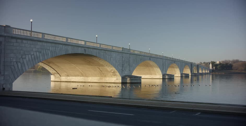 Flock of ducks swimming under an arched stone bridge on a river at sunset
