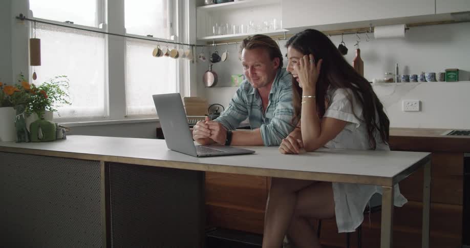 A man and woman laugh as they look at a laptop while at home