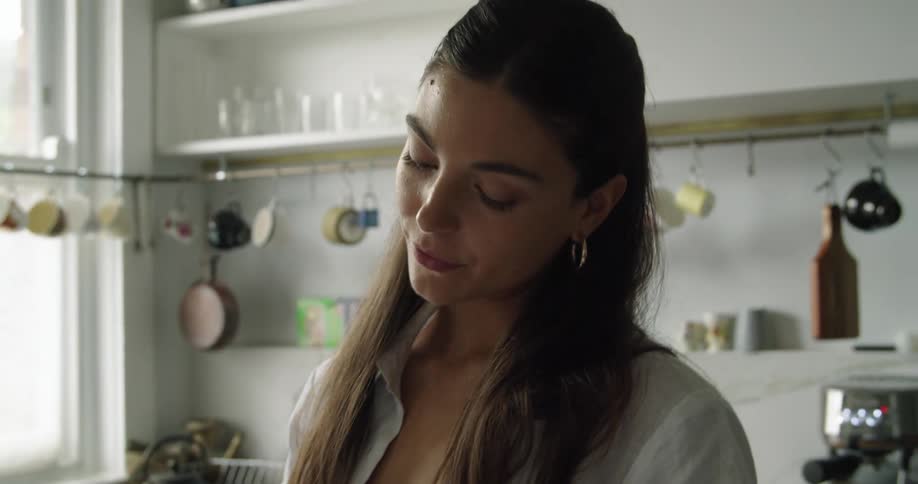 A woman standing in the kitchen using a smart phone with a window in the background