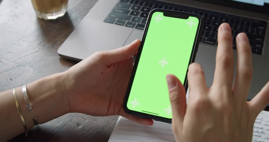 A woman sitting at a table swipes her finger across the screen of a smartphone