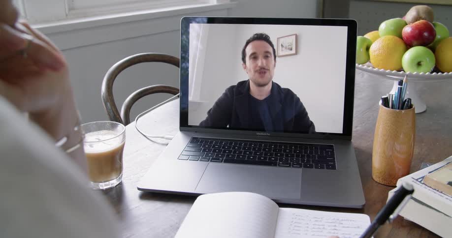 A woman takes notes as she video chats with a professor