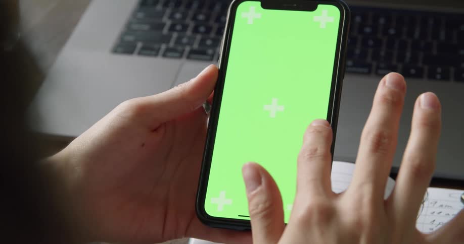A person sits in front of the their laptop and scrolls on their cell phone