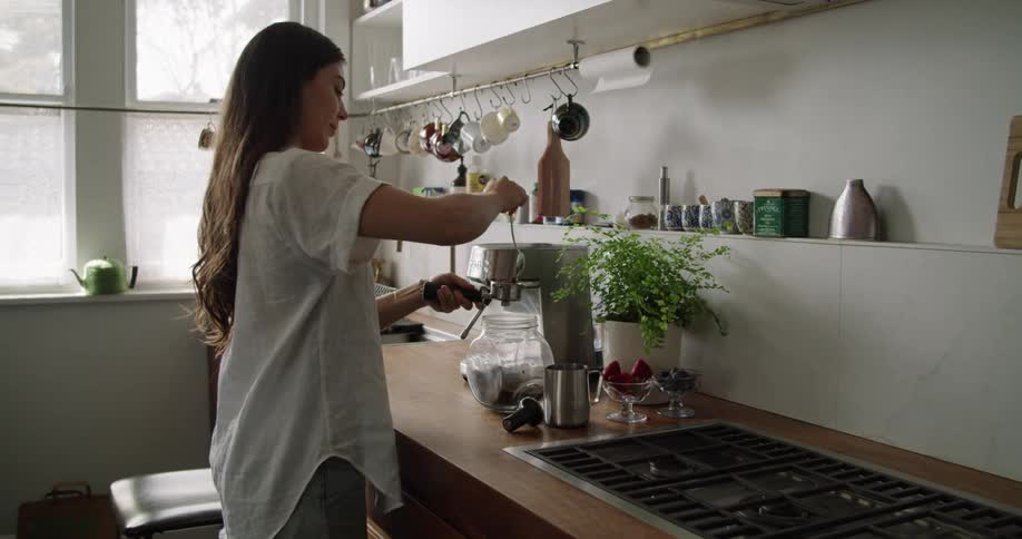 A woman in a kitchen scooping coffee grinds with a spoon into a cylinder