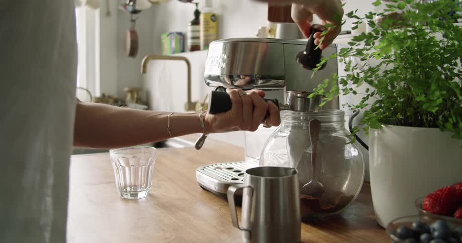 A person uses a coffee grinder to prepare coffee in a home kitchen during the day