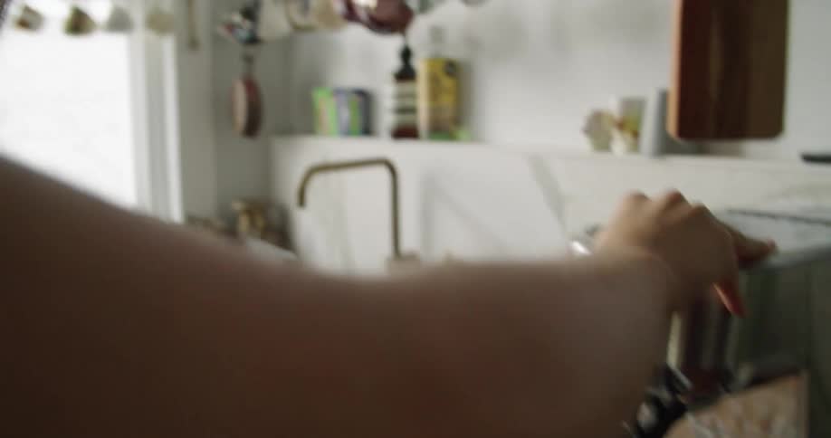 Young woman uses the milk frother attached to the spresso machine on the kitchen countertop at home