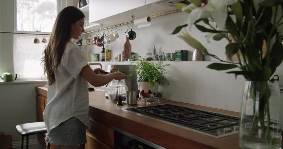 Young woman pouring coffee grounds on an espresso machine in the kitchen countertop at home
