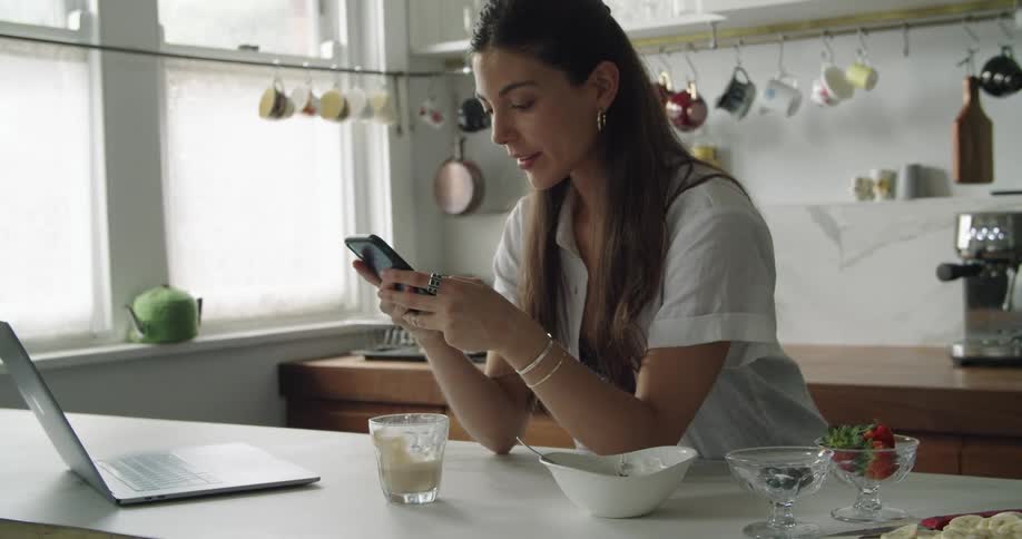 A woman stands in a kitchen texting on her cell phone