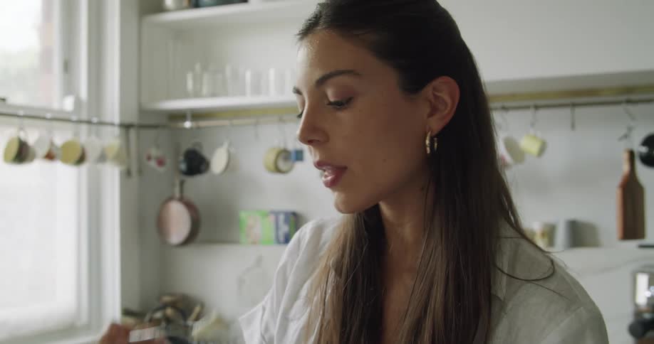 A woman standing in the kitchen eating a bowl of fruit