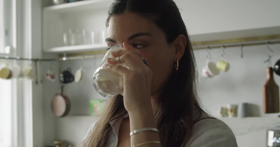Young woman having breakfast in the kitchen at home types a message on her smartphone