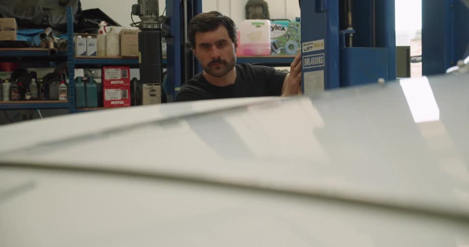 A man in large garage lowers a car on a powered car lift