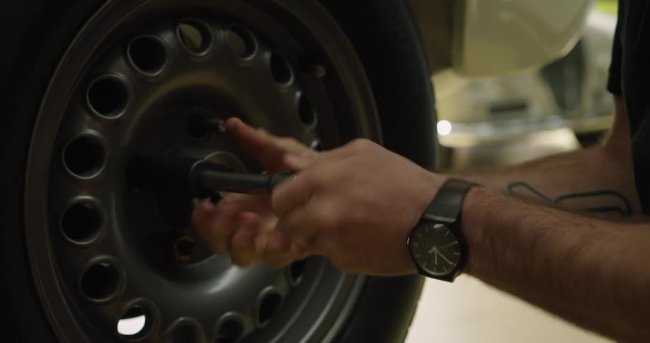 Man using a tool on a tire screw on a white car in a mechanic workshop