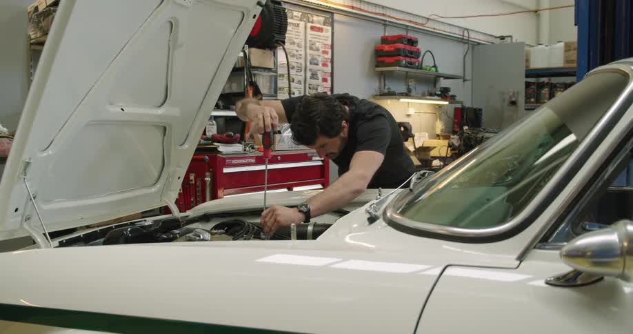 Man works in garage on car engine using screwdriver