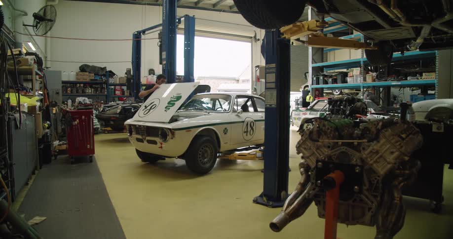 A mechanic in a shop opens the hood of a car