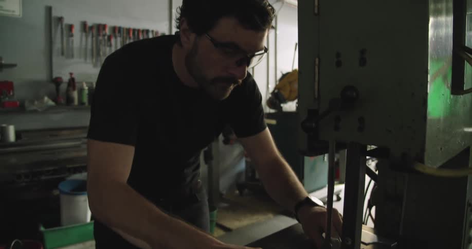 A man wearing safety glasses uses a band saw to cut a plastic sheet