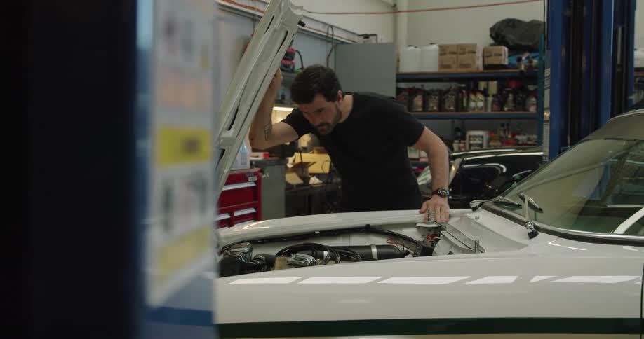 A mechanic opens the hood of a car and looks underneath