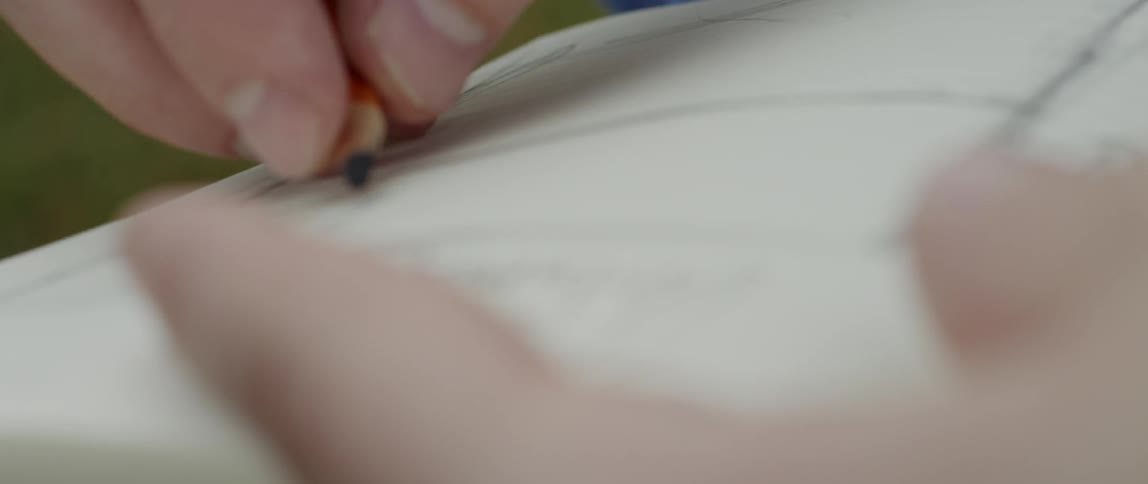 A man's hands are shown drawing with pencil in a notebook