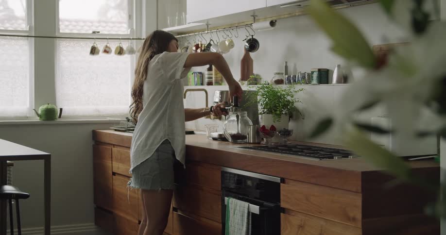 A woman in a kitchen scooping coffee grinds into a cylinder and placing it into a coffee machine